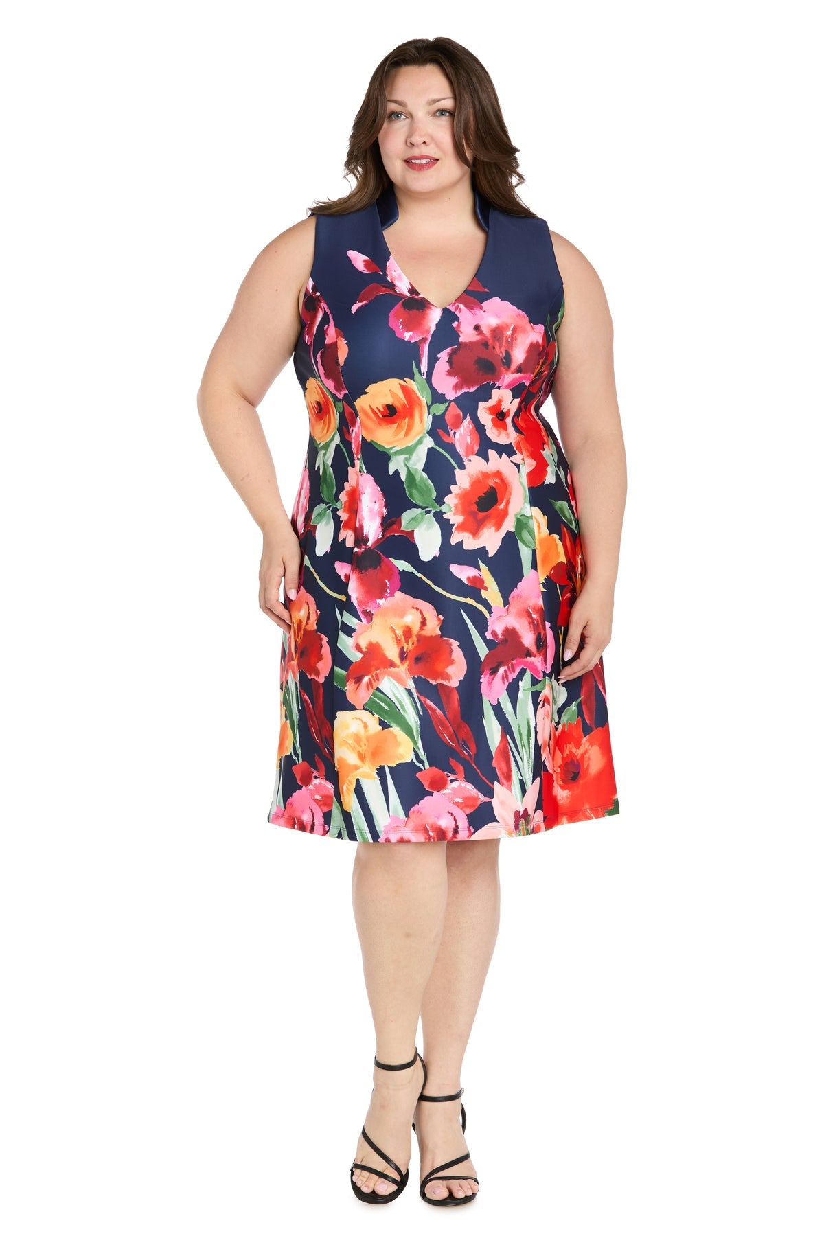 A woman wears the R&M Richards 4056W Plus-Size Wedding Guest Dress—a sleeveless, knee-length floral dress—standing facing forward against a white background, perfect for any semi-formal occasion.